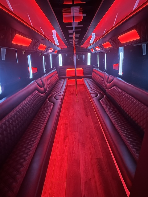Party bus interior with red LED lighting, diamond-stitched leather seating and dance pole
